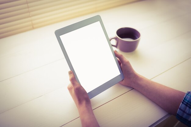 Mãos segurando comprimido digital por xícara de café na mesa