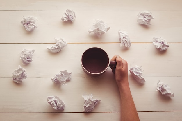 Mãos segurando copo de café ao lado de bolas de papel