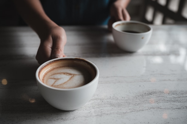 Mãos segurando duas xícaras brancas de café quente na mesa de café