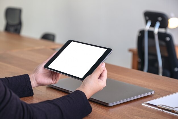 mãos segurando e usando tablet pc preto com tela de desktop em branco branco com notebook na mesa de madeira no escritório