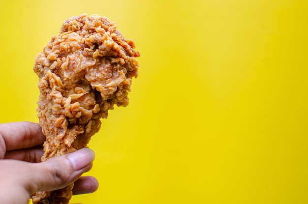 Mãos segurando frango frito isolado em fundo amarelo saboroso batom de frango frito crocante