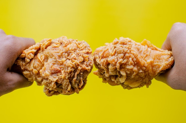 Foto mãos segurando frango frito isolado em fundo amarelo saboroso batom de frango frito crocante