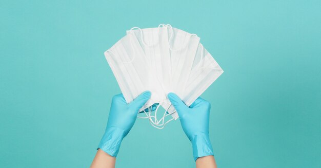 Mãos segurando máscaras usam luvas médicas azuis ou luvas de látex com fundo verde ou azul Tiffany.