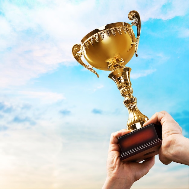 Mãos segurando o troféu de ouro no fundo do céu azul