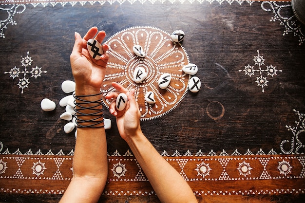 Foto mãos segurando pedras rúnicas em uma mesa ornamentada