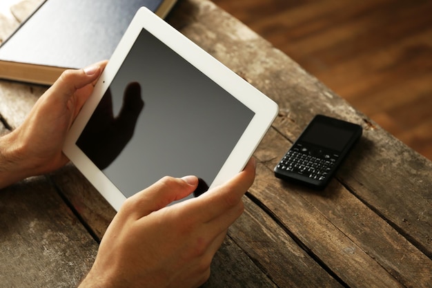 Mãos segurando tablet digital em fundo de mesa de madeira