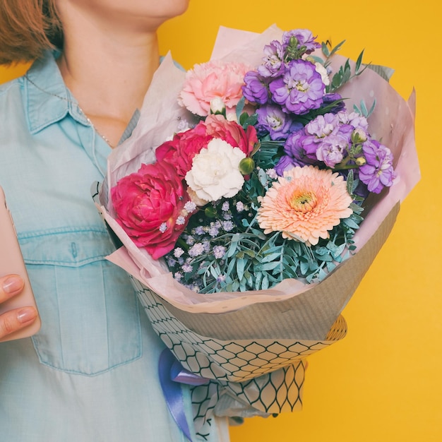 Mãos segurando um buquê de lindas flores sobre fundo amarelo. Imagem tonificada