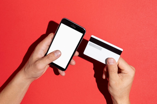 Mãos segurando um cartão de crédito e um telefone simulado