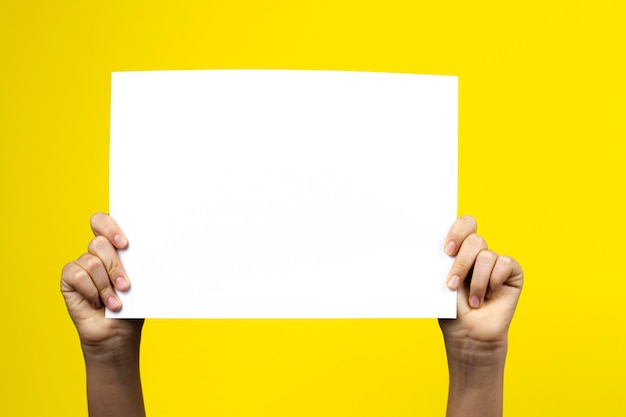 Mãos segurando um cartaz de papel em branco na parede amarela