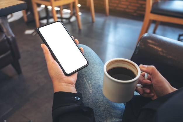 Mãos segurando um celular branco com tela em branco enquanto bebe café em um café moderno