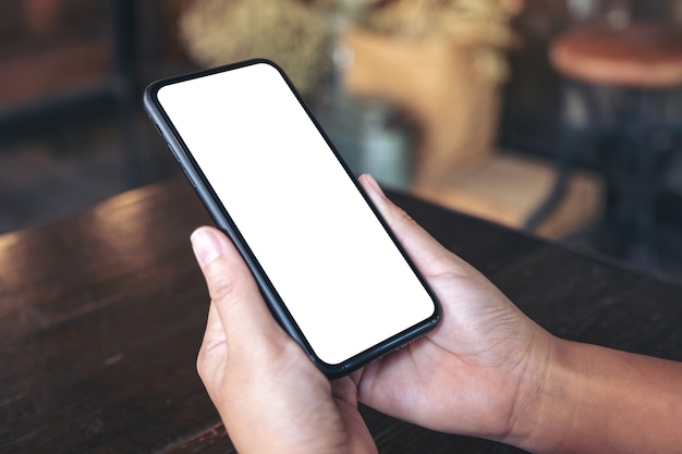 Mãos segurando um celular preto com uma tela branca em branco em um café vintage