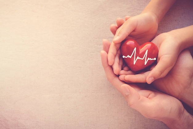 Mãos segurando um coração vermelho com eletrocardiograma, conceito de saúde do coração