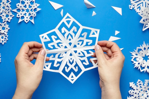 Mãos segurando um floco de neve de papel cortado branco na superfície azul