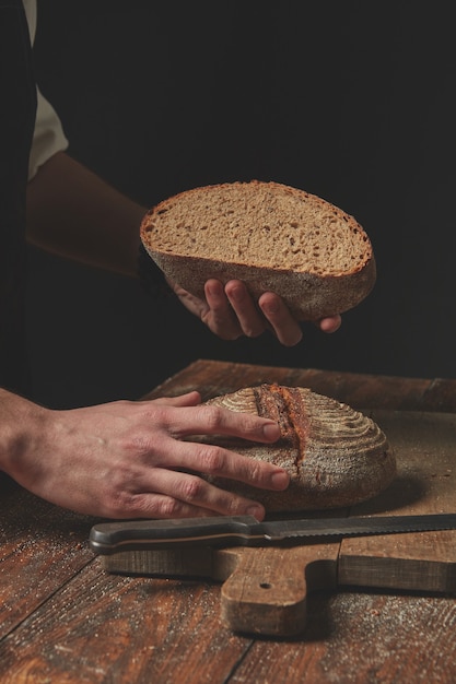 Mãos segurando um pedaço de pão assado em fundo escuro