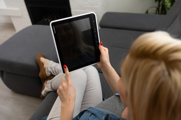 mãos segurando um tablet inteligente com app casa inteligente na sala de estar como pano de fundo.