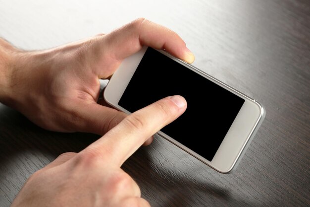 Mãos segurando um telefone celular inteligente no fundo da mesa de madeira