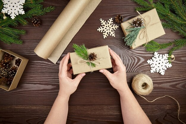 Mãos segurando uma caixa de presente de natal decorada na mesa de madeira