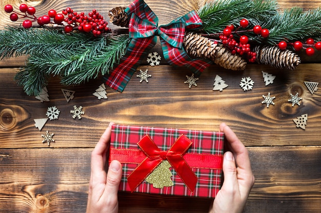 Mãos segurando uma caixa de presente em um fundo de madeira de Natal. Ano novo, clima de férias, árvore de Natal, flocos de neve, cones. copyspace, eco amigável, plana leigos. Embalagem de férias