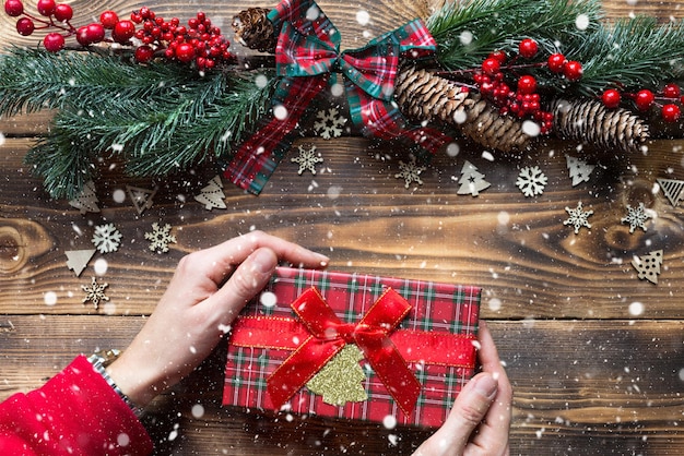 Mãos segurando uma caixa de presente em um fundo de madeira de Natal. Ano novo, clima de férias, árvore de Natal, flocos de neve, cones. copyspace, eco amigável, plana leigos. Embalagem de férias