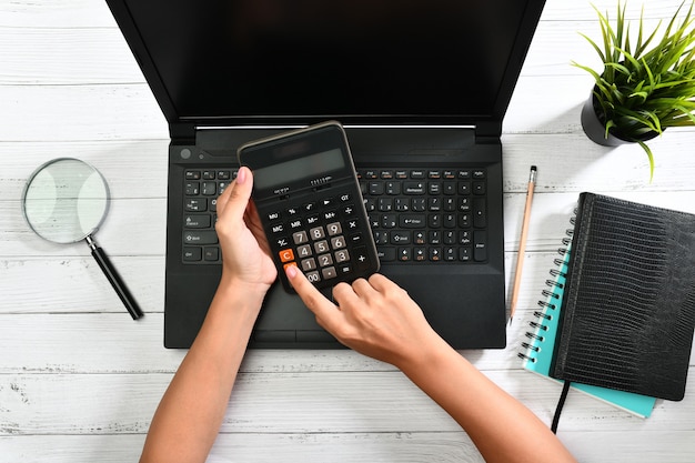 Mãos segurando uma calculadora sobre um laptop