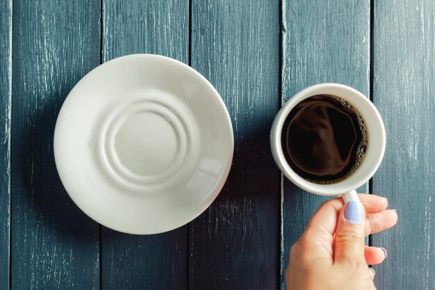 Mãos segurando uma caneca de bebida quente na mesa de madeira