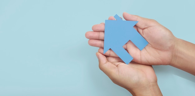 Mãos segurando uma casa de papel, uma casa de família e protegendo o conceito de seguro