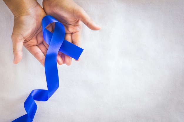 Foto mãos segurando uma fita azul profunda em tecido branco com espaço de cópia conscientização do câncer colorretal câncer de cólon de pessoa idosa e dia mundial da diabetes prevenção do abuso infantil conceito de seguro de saúde