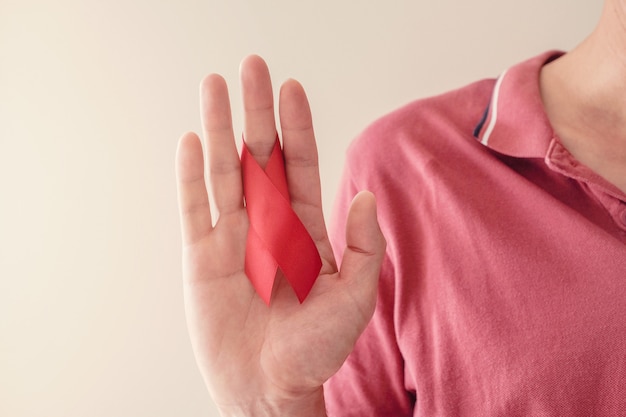 Mãos segurando uma fita vermelha sobre fundo vermelho, conceito de conscientização do hiv, dia mundial da Aids