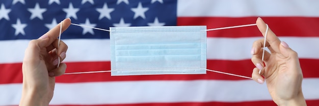 Mãos segurando uma máscara médica protetora na frente da bandeira dos EUA nova cepa do conceito de coronavírus