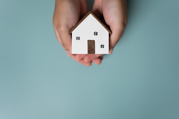 Mãos segurando uma pequena casa de madeira conceito de proteção ou economia para novo projeto residencial