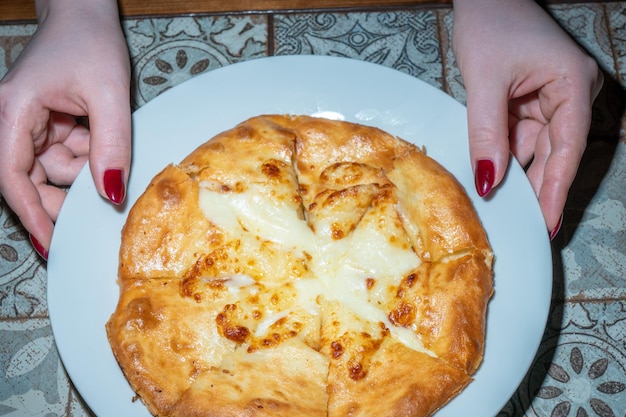 Mãos segurando uma pizza com a mão superior esquerda segurando um pedaço de queijo.