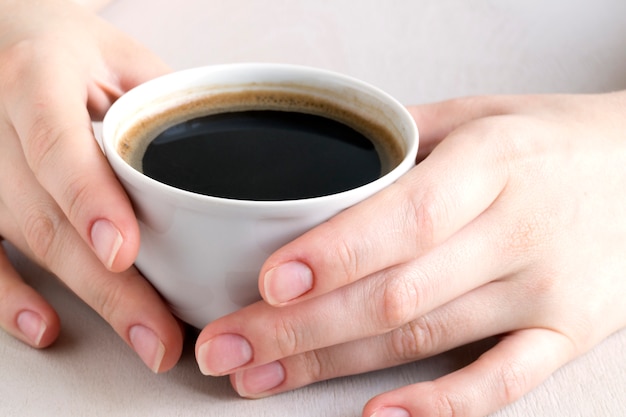 Mãos segurando uma xícara de café em uma mesa brilhante.