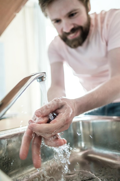 Mãos sob um fluxo de água limpa sorrindo homem observando as regras de higiene