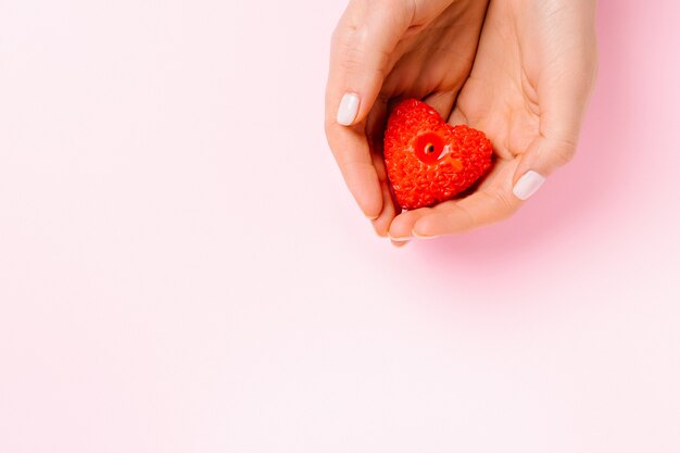 Mãos suaves com uma vela em forma de coração em um fundo rosa com espaço em branco.