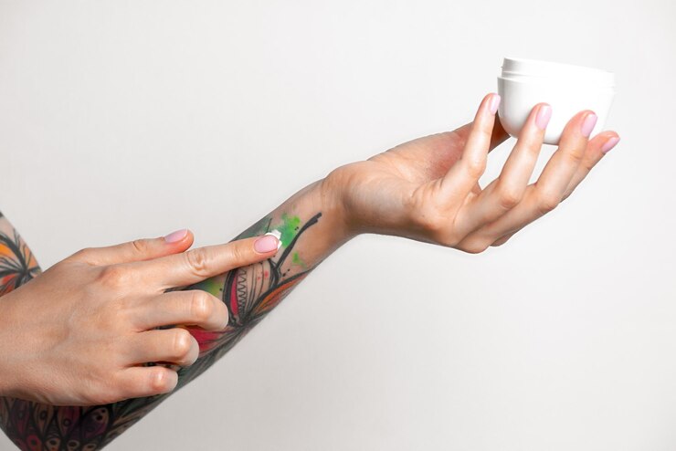 Foto mãos tatuadas femininas seguram um frasco de creme dedos aplicam creme na pele