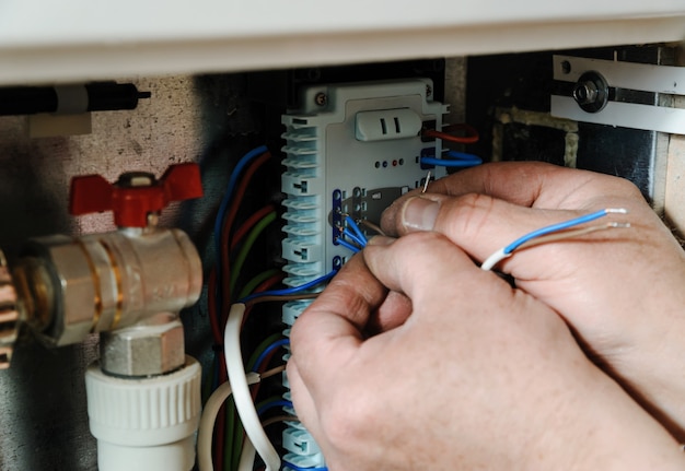 Mãos trocando fios de sinal no controle do sistema de aquecimento doméstico.