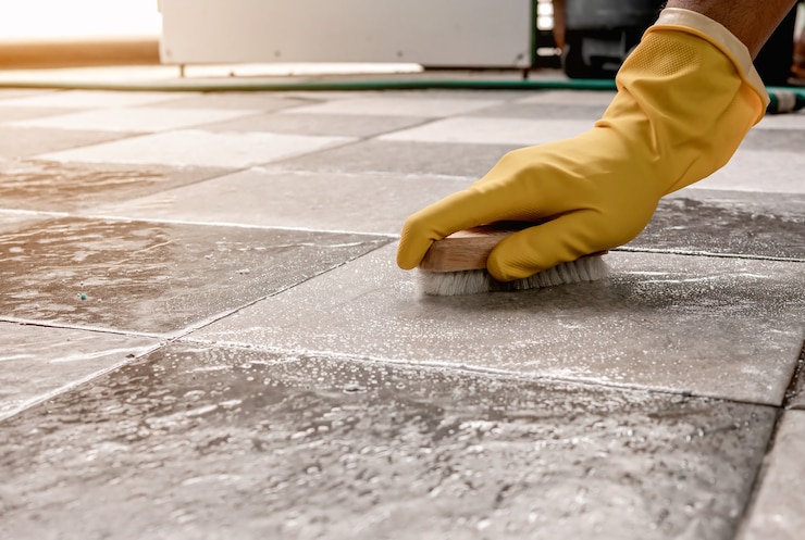 Foto mãos usando luvas de borracha amarelas estão usando um limpador de piso de madeira para esfregar o piso de ladrilhos com um limpador de piso.
