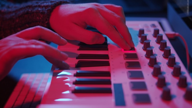 Foto mãos usando teclado midi em home studio à noite com luzes de neon