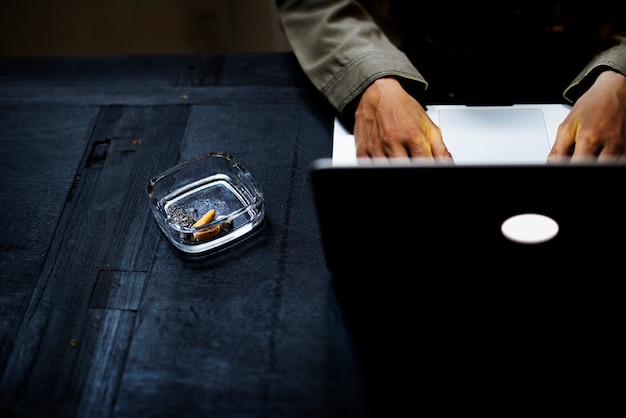 Mãos usando um laptop com um cigarro no cinzeiro