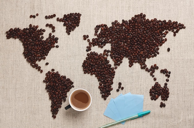 Mapa do mundo feito de grãos de café torrados. xícara de café e notas para escrever