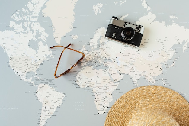 Mapa-múndi mínimo com alfinetes, câmera retro, óculos de sol, chapéu de palha