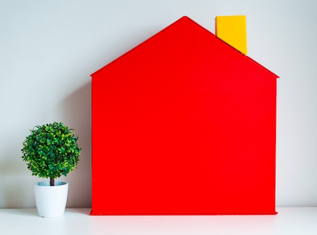 Maqueta de un árbol de casa de casa roja de juguete en una pared blanca ideas de conceptos de propiedad y finca o inversión