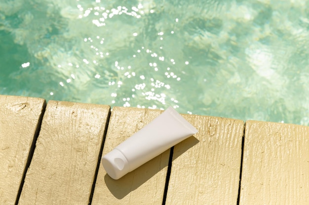 Maqueta blanca de un tubo de crema hidratante facial o protector solar en una piscina con deslumbramiento solar El concepto de cosméticos de cuidado de belleza para el cuerpo