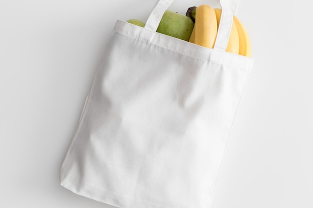 Maqueta de bolso de mano blanco con fruta en una mesa blanca