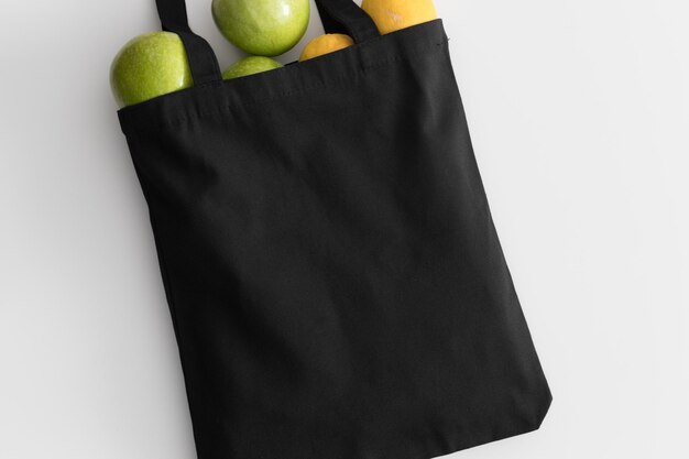 Foto maqueta de bolso de mano negro con fruta en una mesa blanca