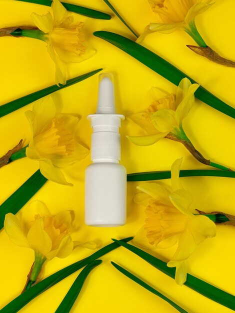 Maqueta de botella de aerosol nasal médica blanca sobre fondo amarillo flores de narciso planas Remedio contra la alergia a la fiebre del heno
