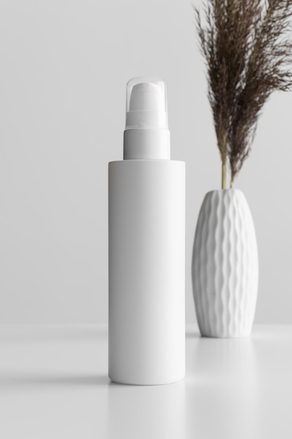 Maqueta de botella de loción cosmética blanca con una flor seca en la mesa blanca