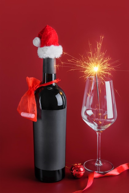 Maqueta de botella de vino tinto con etiqueta negra con Santa Claus rojo y copa de vino con bengalas. Enfoque selectivo. Feliz Navidad y un próspero año nuevo concepto festivo de invierno