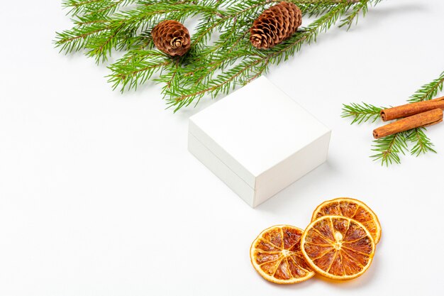 Maqueta caja de regalo blanca con frutos secos de naranja, canela, cono, ramita de abeto árbol de Navidad en blanco