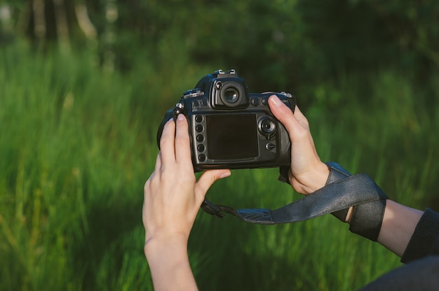 Maqueta de una cámara de foto-video profesional en manos de una niña. En el contexto de la naturaleza verde.